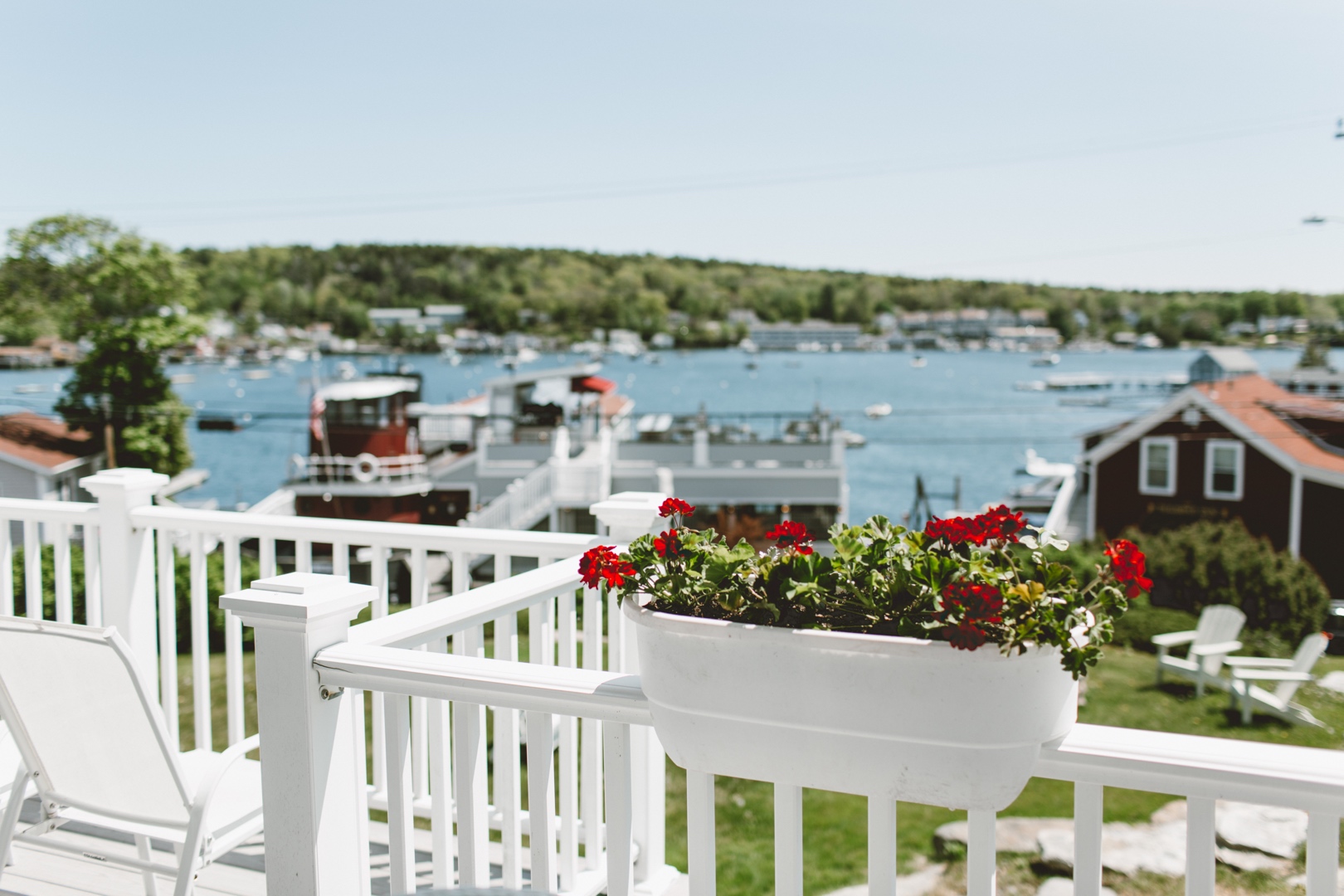a white railing with red flowers and boats in the background